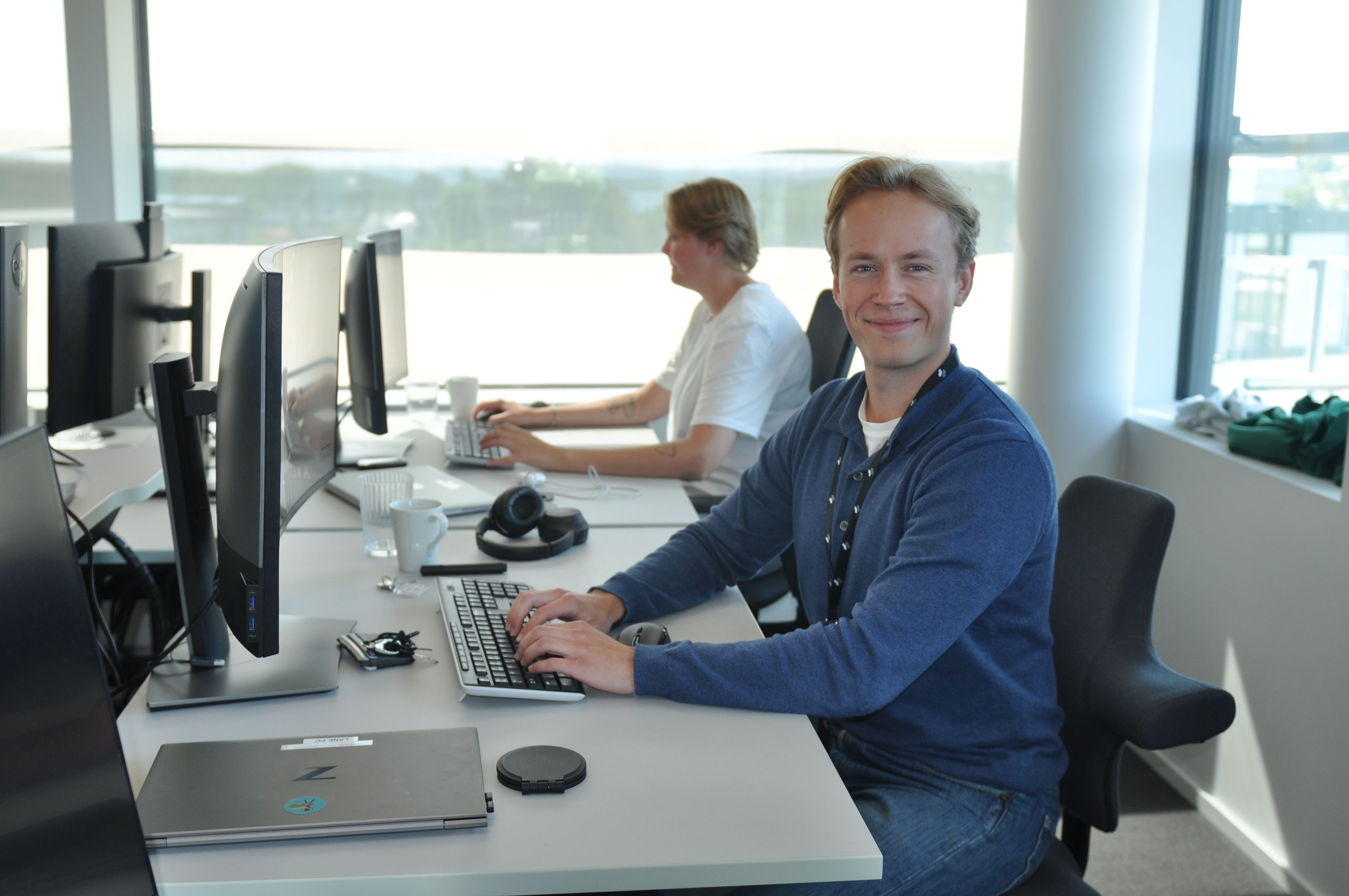 Sommerstudent Johannes sitter smilende ved en pult med hendene på et keyboard og ved siden av en annen sommerstudent
