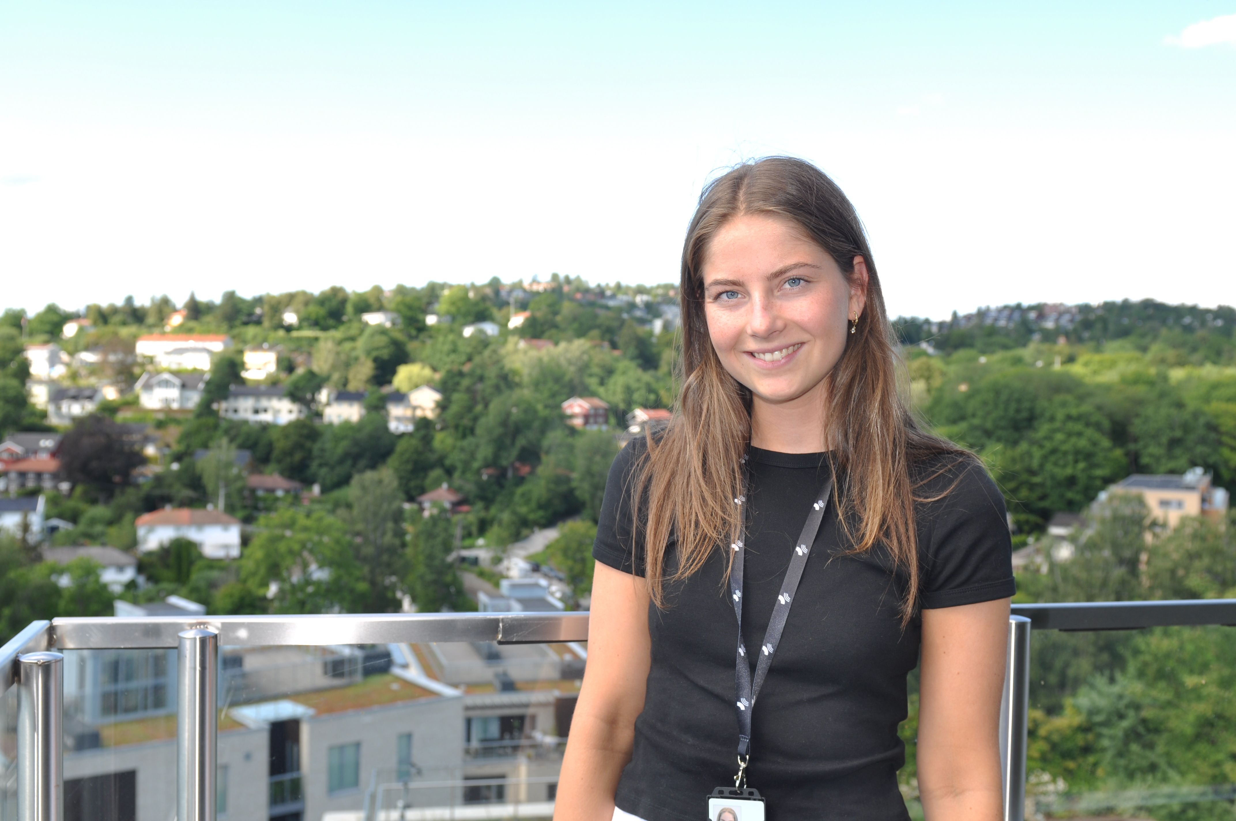Sommerstudent Ingrid står smilende på en terrasse med utsikt over en grønn skog
