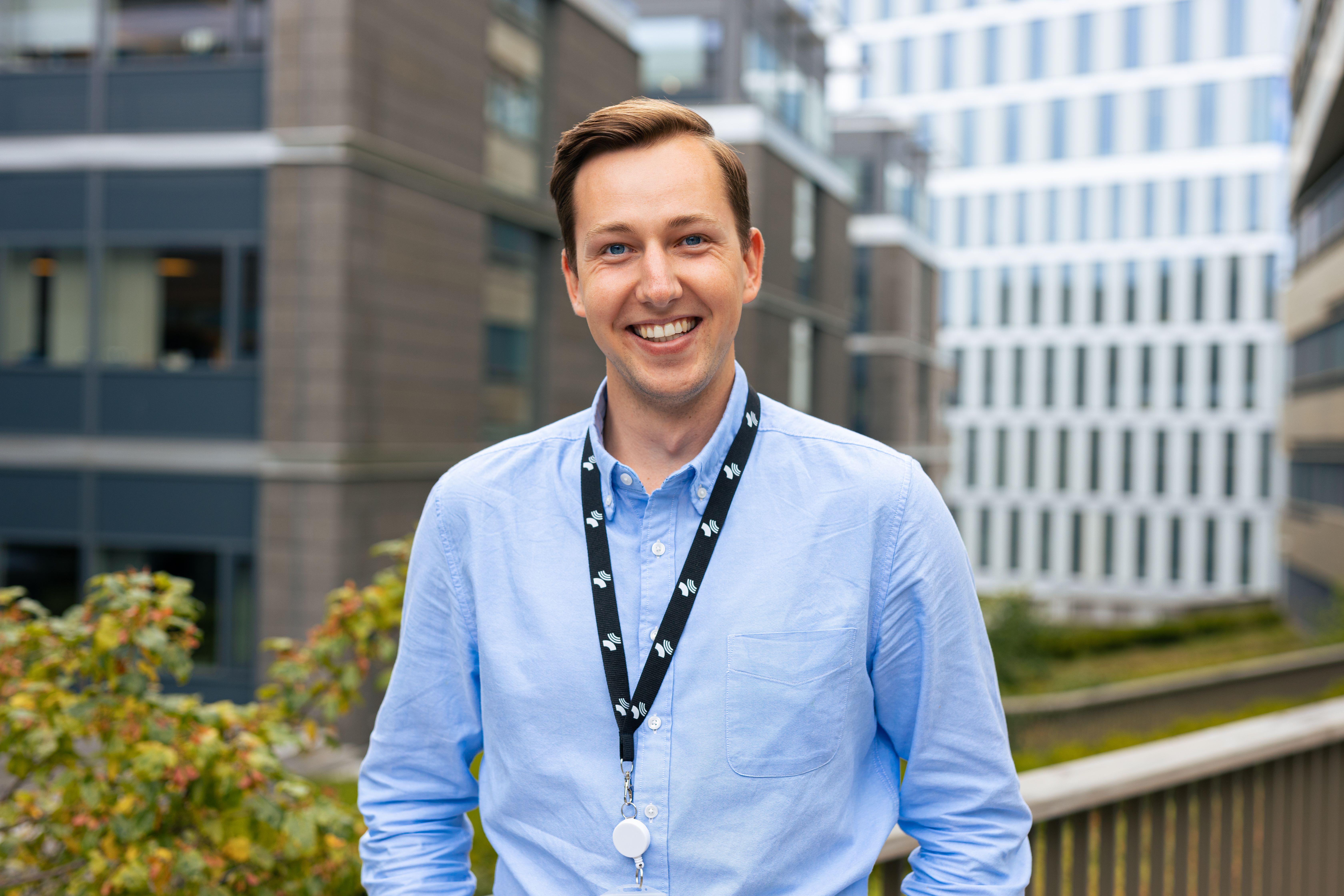 Smilende mann i skjorte utenfor noen bygg