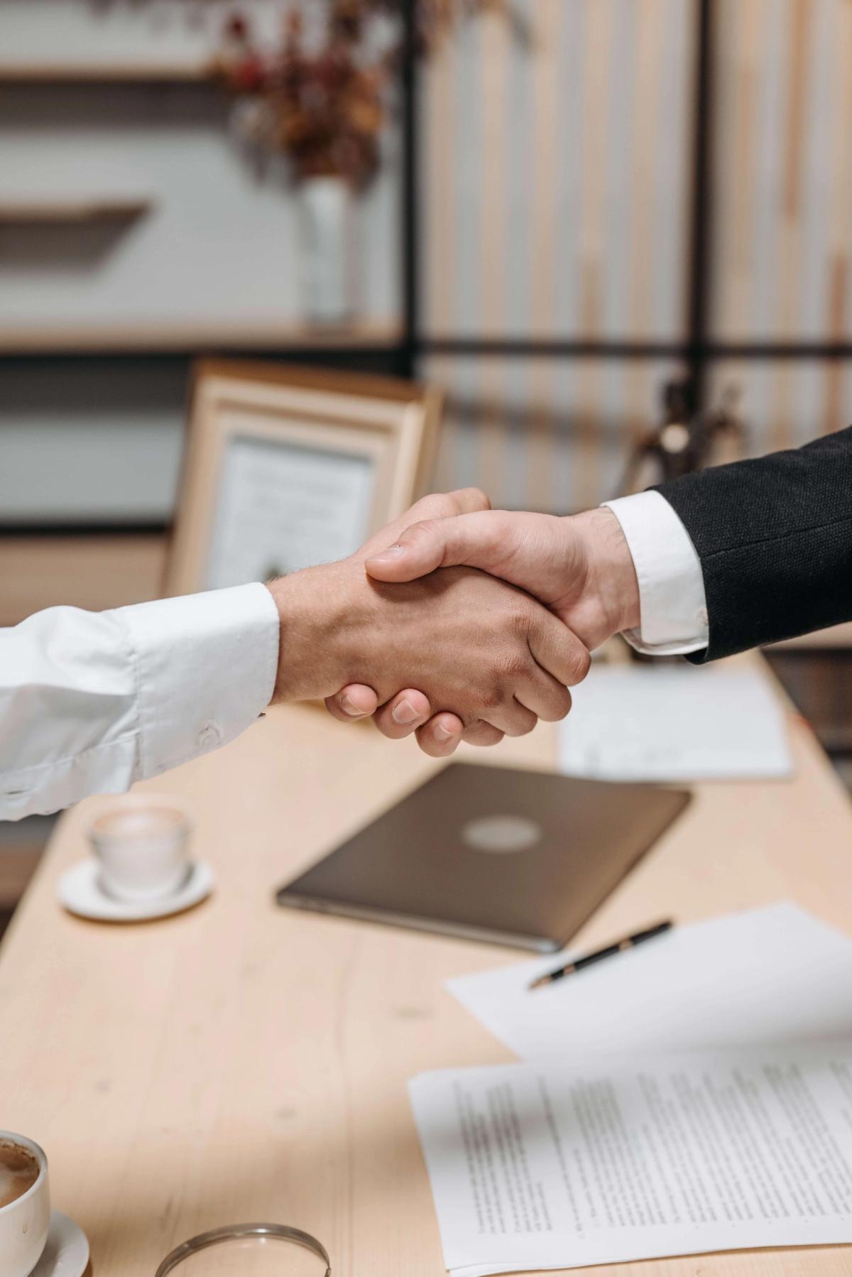 Two people shaking hands across a table after reaching an agreement