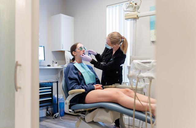 A dentist in a mask and gloves works on a patient's teeth in a dental chair.