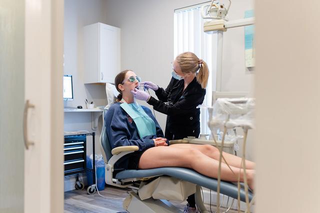 a woman is sitting in a dental chair getting her teeth examined by a dentist .
