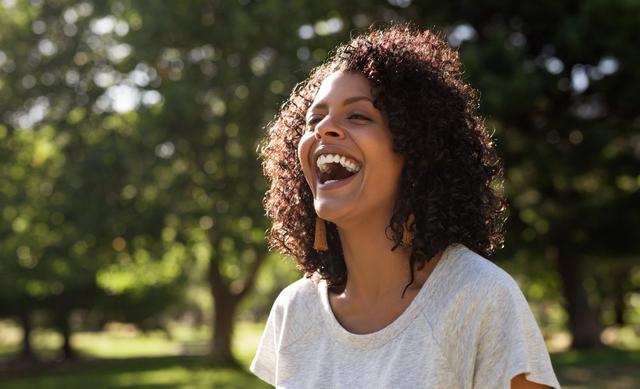 a woman is laughing in a park with her mouth open .