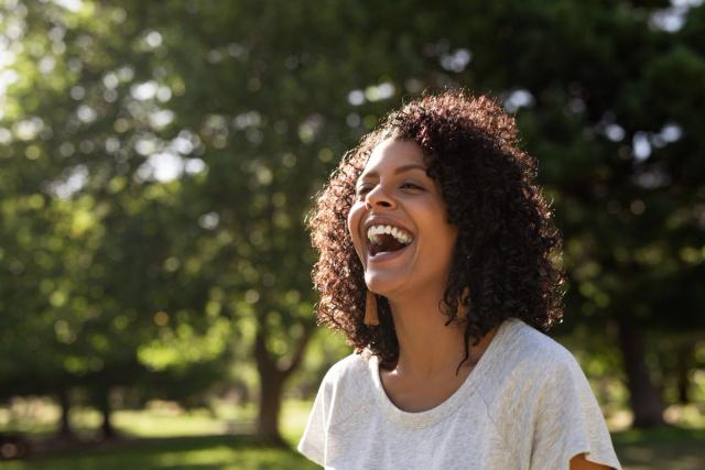 a woman is laughing in a park with her mouth open .