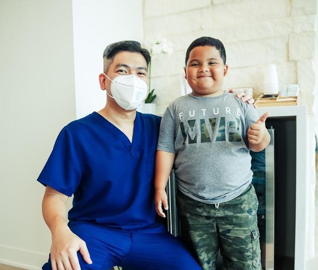 a man wearing a mask is sitting next to a young boy who is giving a thumbs up .