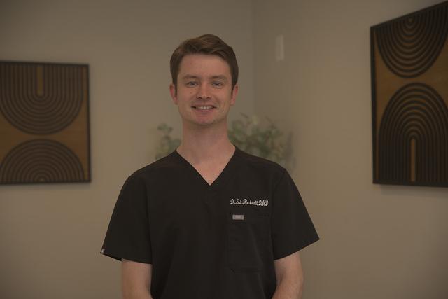 Dr. Eric Rickett D.M.D. smiling in black scrubs.