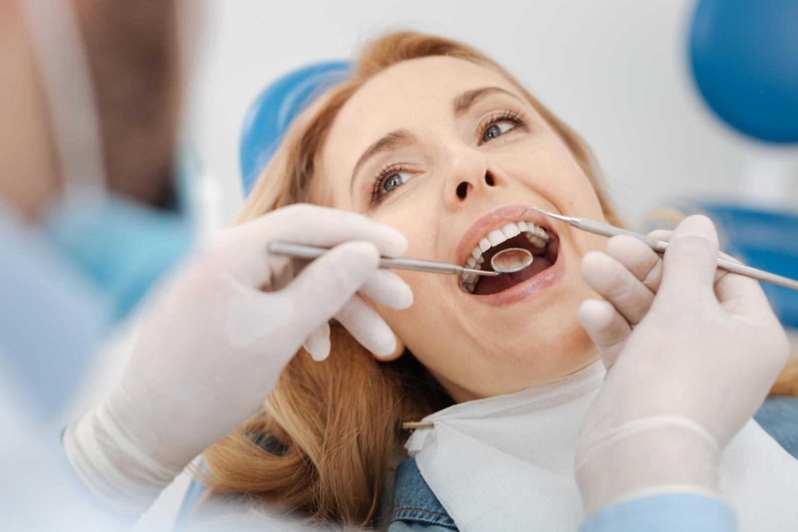 A woman in a dental chair having her teeth examined by a dentist.