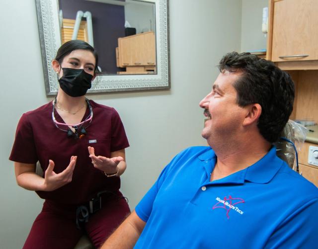 a woman in a mask is talking to a man in a blue shirt in a dental office .