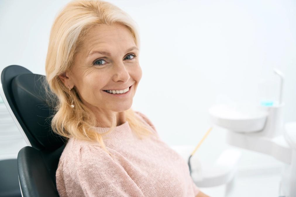 a woman is smiling while sitting in a dental chair.