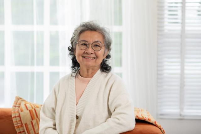 an elderly woman is sitting on a couch wearing glasses and smiling .