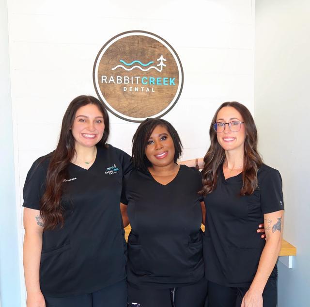 three female dental assistants are posing for a picture in front of a rabbit creek dental sign .