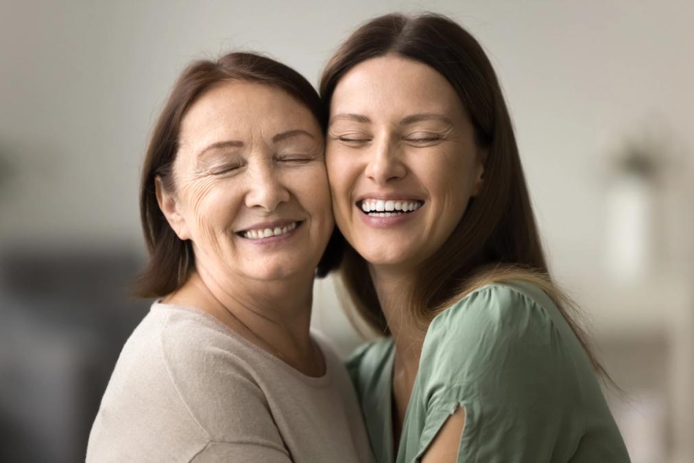 An older woman and a younger woman embracing and smiling happily with closed eyes.