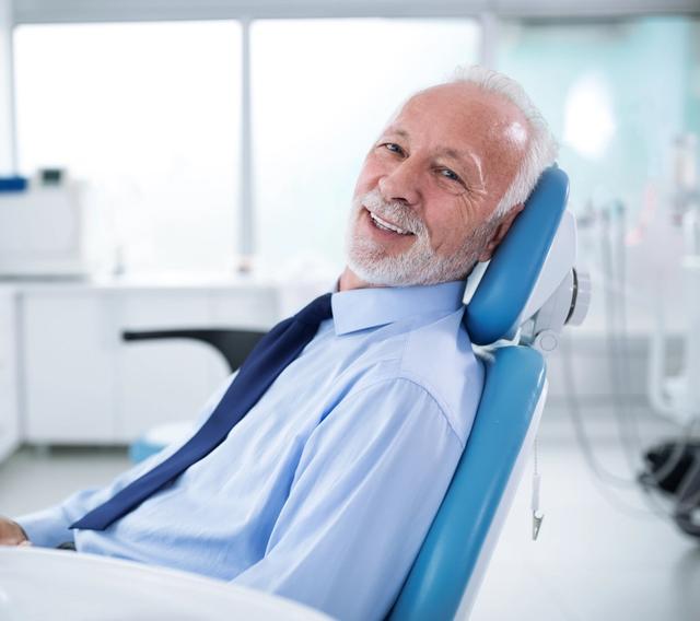 an older man is sitting in a dental chair and smiling .