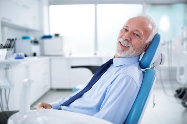an older man is sitting in a dental chair and smiling .