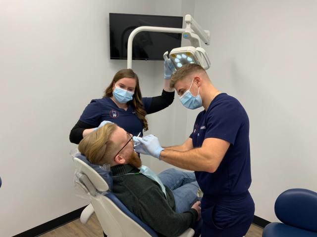 a man is sitting in a dental chair getting his teeth examined by two dentists .