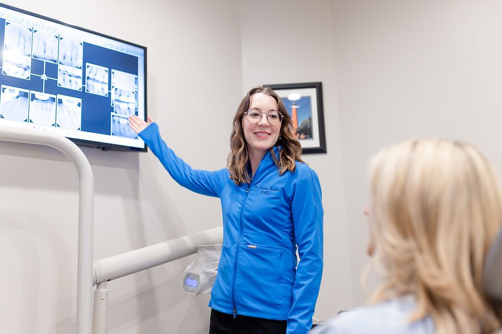 A dentist points to dental X-rays on a monitor while consulting with a patient.