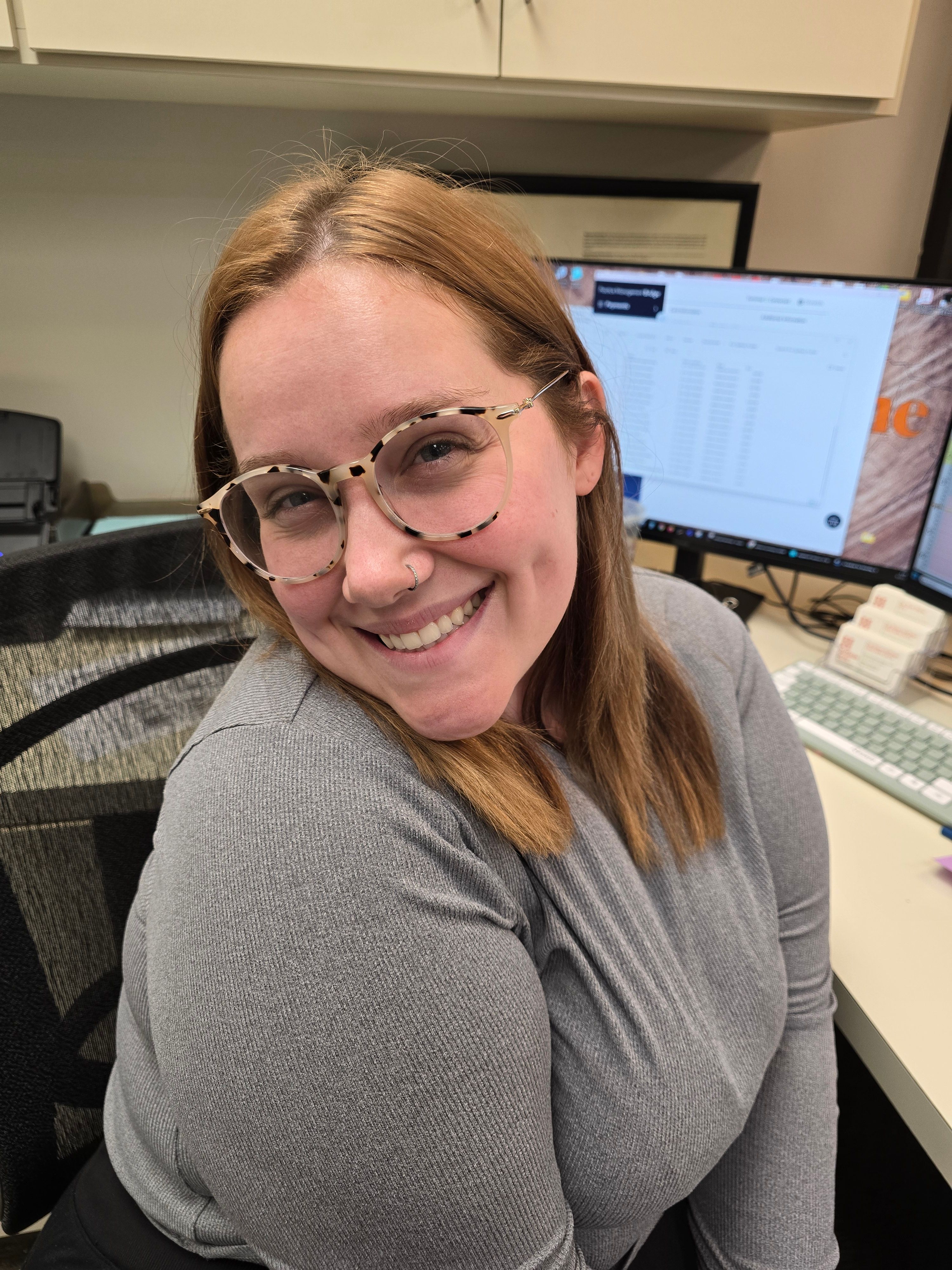 a woman wearing glasses is smiling while sitting at a desk in front of a computer .