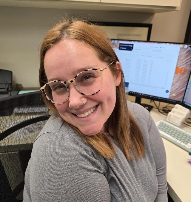 a woman wearing glasses is smiling while sitting at a desk in front of a computer .