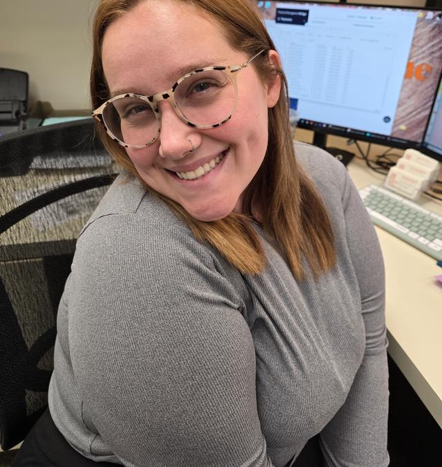 a woman wearing glasses is smiling while sitting at a desk in front of a computer .