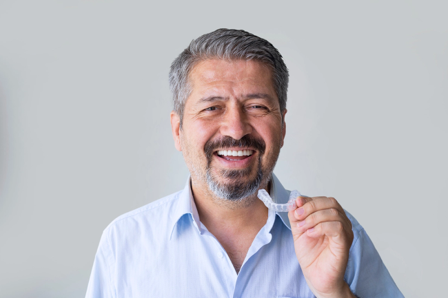 a man in a blue shirt is smiling and holding a clear mouth guard