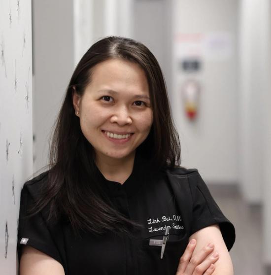 a woman in a black scrub top is leaning against a wall and smiling .