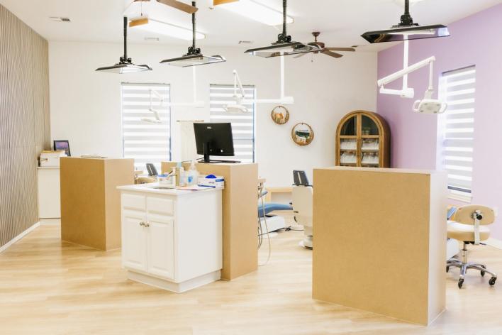 A bright, modern dental office with multiple treatment bays, light wood floors, and white and light purple walls.