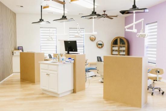 A modern, open-concept dental or orthodontic office with multiple treatment bays, light wood floors, and accent walls.