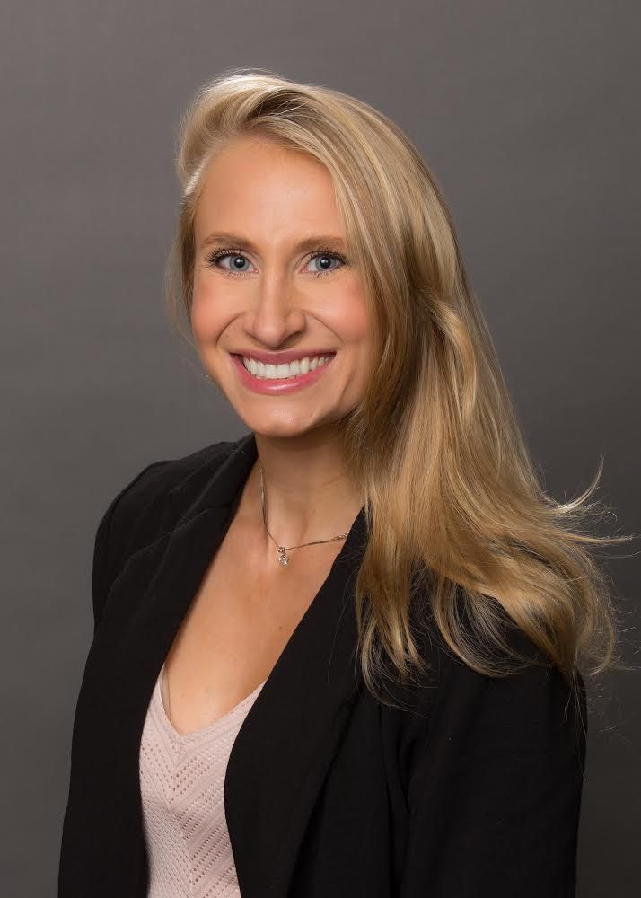 a woman wearing a black jacket and a pink shirt is smiling for the camera .