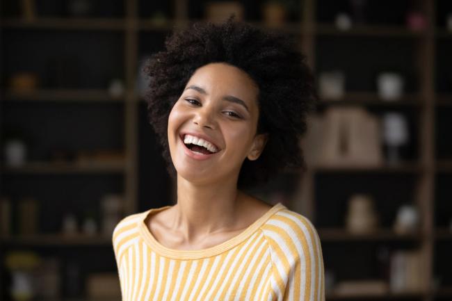 A Black woman with curly hair laughing, wearing a yellow and white striped shirt.