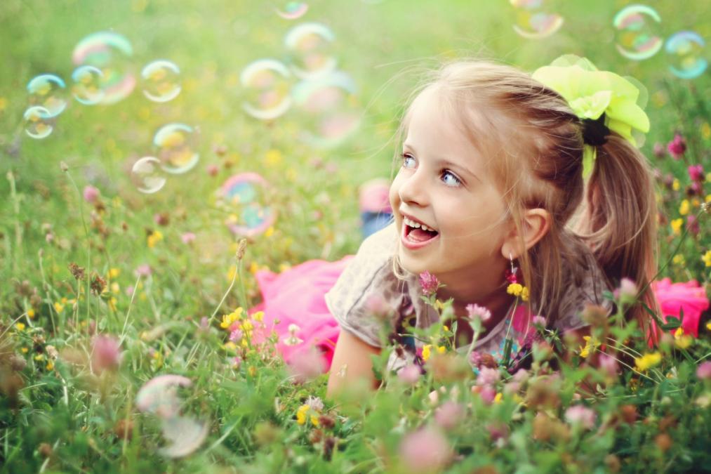a little girl is laying in the grass blowing soap bubbles .