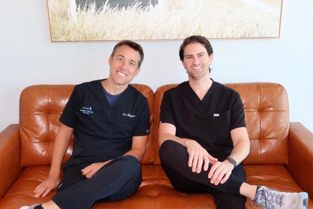 two men in scrubs are sitting on a couch .