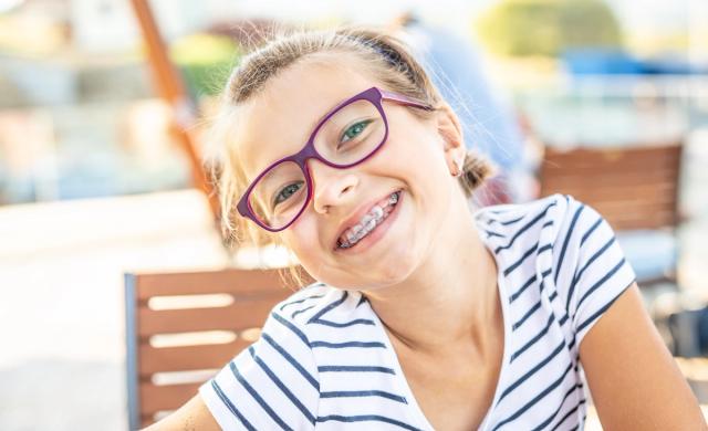 Smiling young girl with purple glasses and braces.