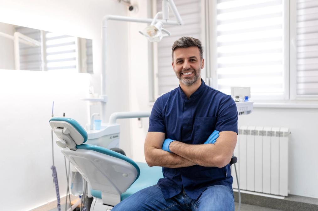 a dentist is sitting in a dental chair with his arms crossed and smiling .