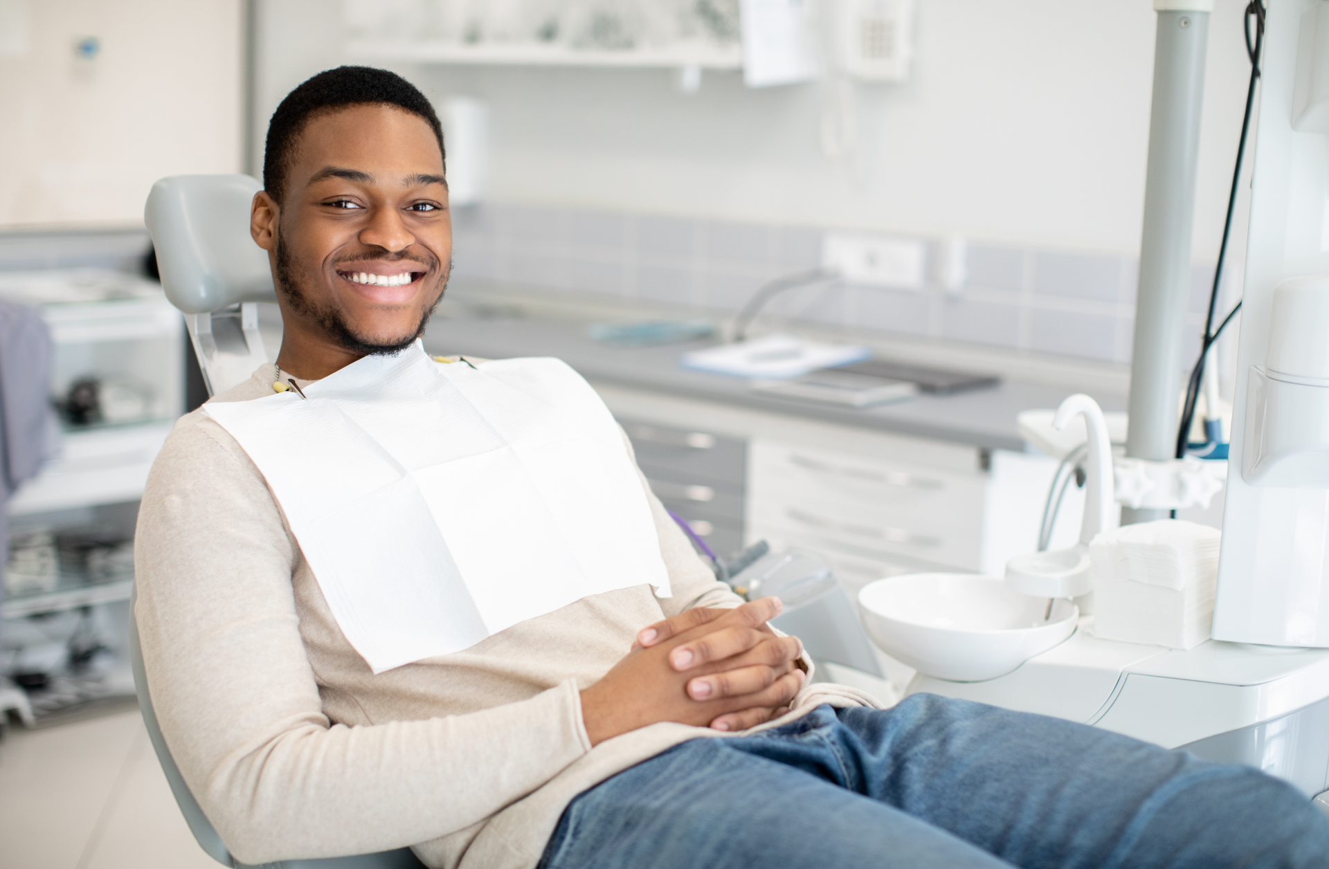 a smiling man sits in a dental chair with his hands folded