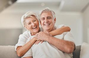 an elderly couple is sitting on a couch hugging each other and smiling .