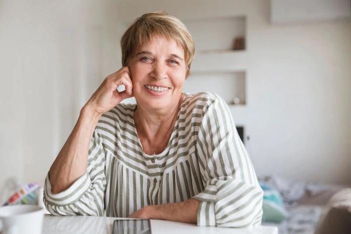 an elderly woman is sitting at a table with her hand on her chin and smiling .