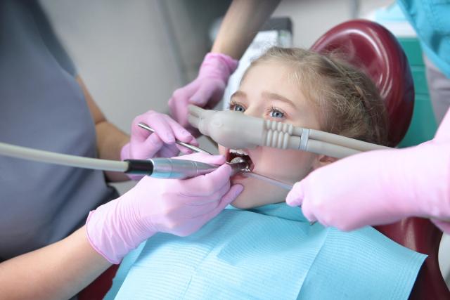 a little girl is getting her teeth examined by a dentist .