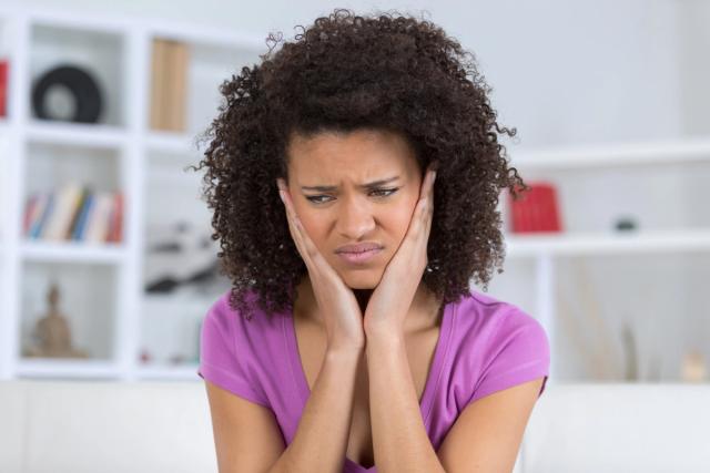 a woman is sitting on a couch with her hands on her face .