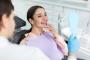 a woman is sitting in a dental chair looking at her teeth in a mirror .