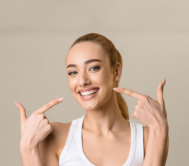 a woman is pointing at her teeth and smiling .