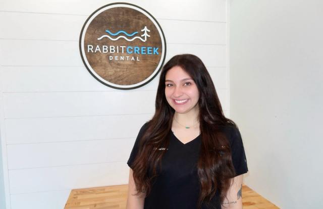 a woman is standing in front of a rabbit creek dental sign .