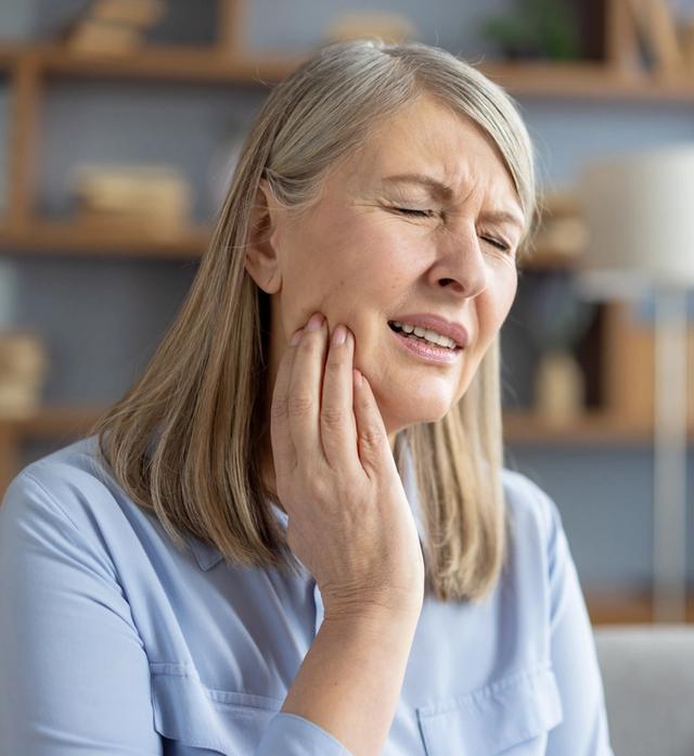 an elderly woman is holding her face in pain because of a toothache .