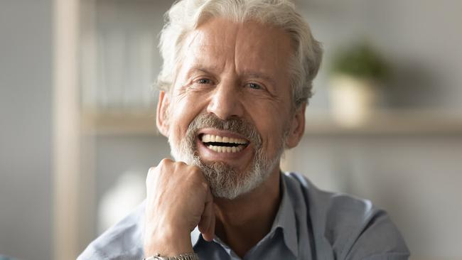 an older man with a beard is smiling with his hand on his chin .