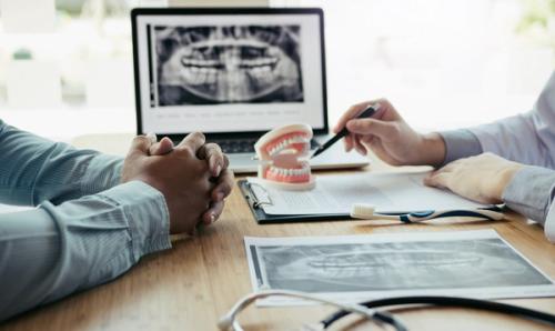 a dentist and a patient are sitting at a table looking at a model of teeth .