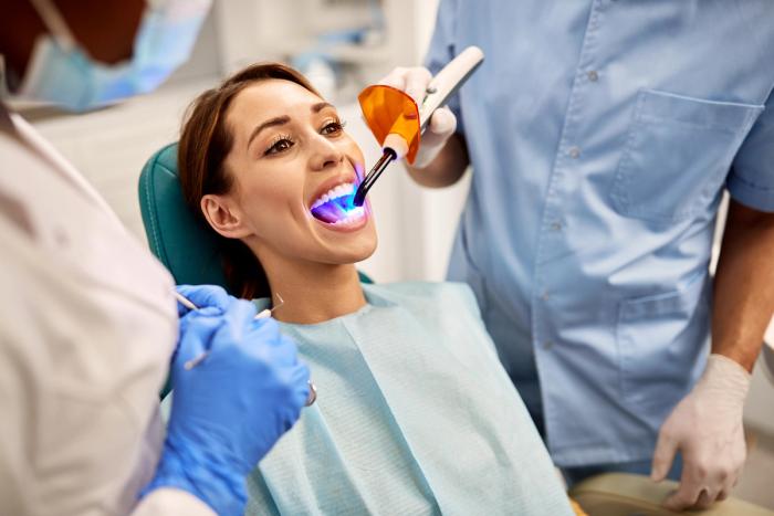 a woman is sitting in a dental chair getting her teeth whitened by a dentist .