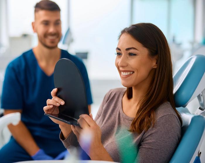 a woman is sitting in a dental chair looking at her teeth in a mirror .