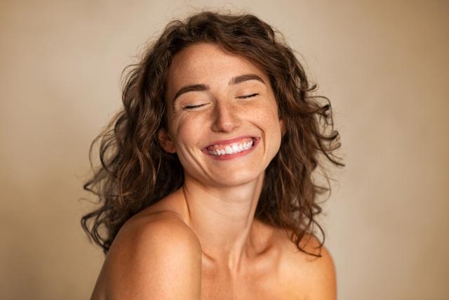 a woman with curly hair is smiling with her eyes closed .