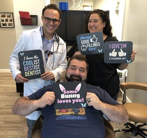 a man is sitting in a dental chair holding a sign that says `` some bunny loves you '' .