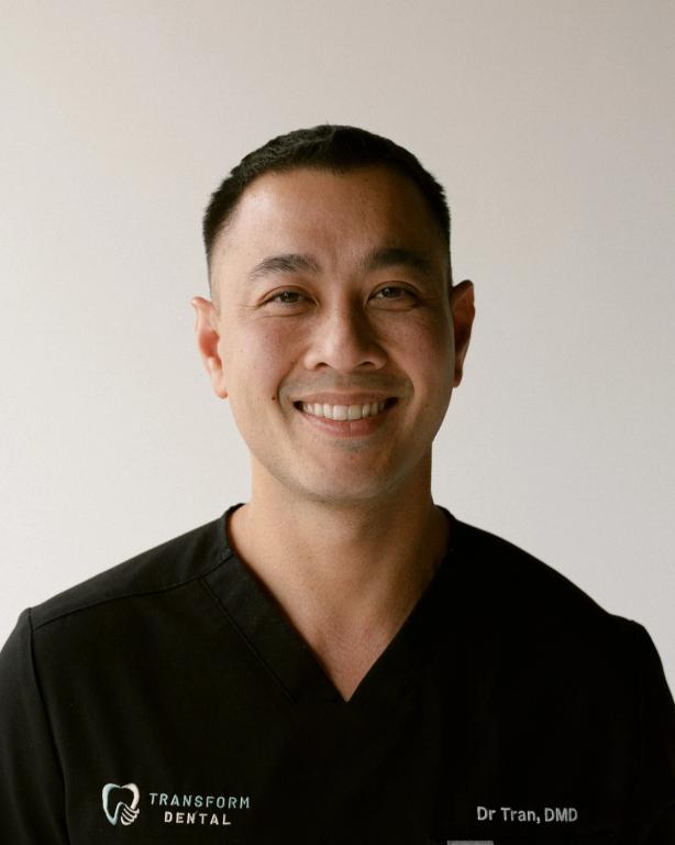 Dr. Tran, DMD, smiling in a black scrub top with the Transform Dental logo.