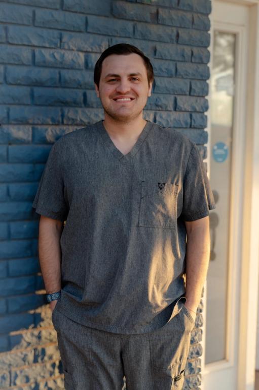 a man standing in front of a blue brick wall wearing a scrub top with the letter s on it